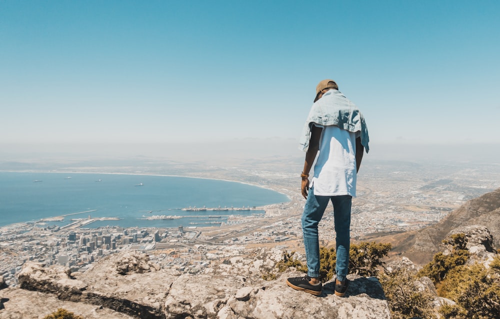 man in blue denim jacket standing on rocky shore during daytime