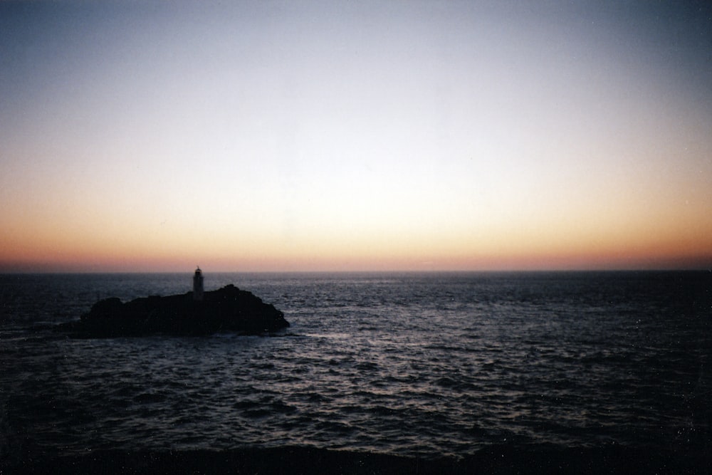 Silhouette einer Person, die während des Sonnenuntergangs auf einem Felsen mitten im Meer steht