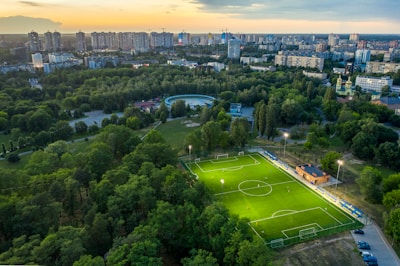 A panoramic view of a city skyline with a football pitch glowing under evening lights.