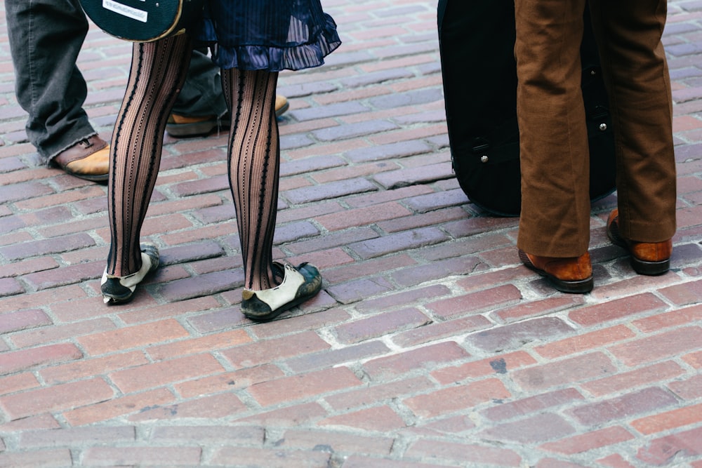 person in black and white checkered pants and black shoes standing on gray concrete brick floor