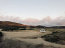 A cozy RV parked beside wildflowers under an open blue sky at sunset.