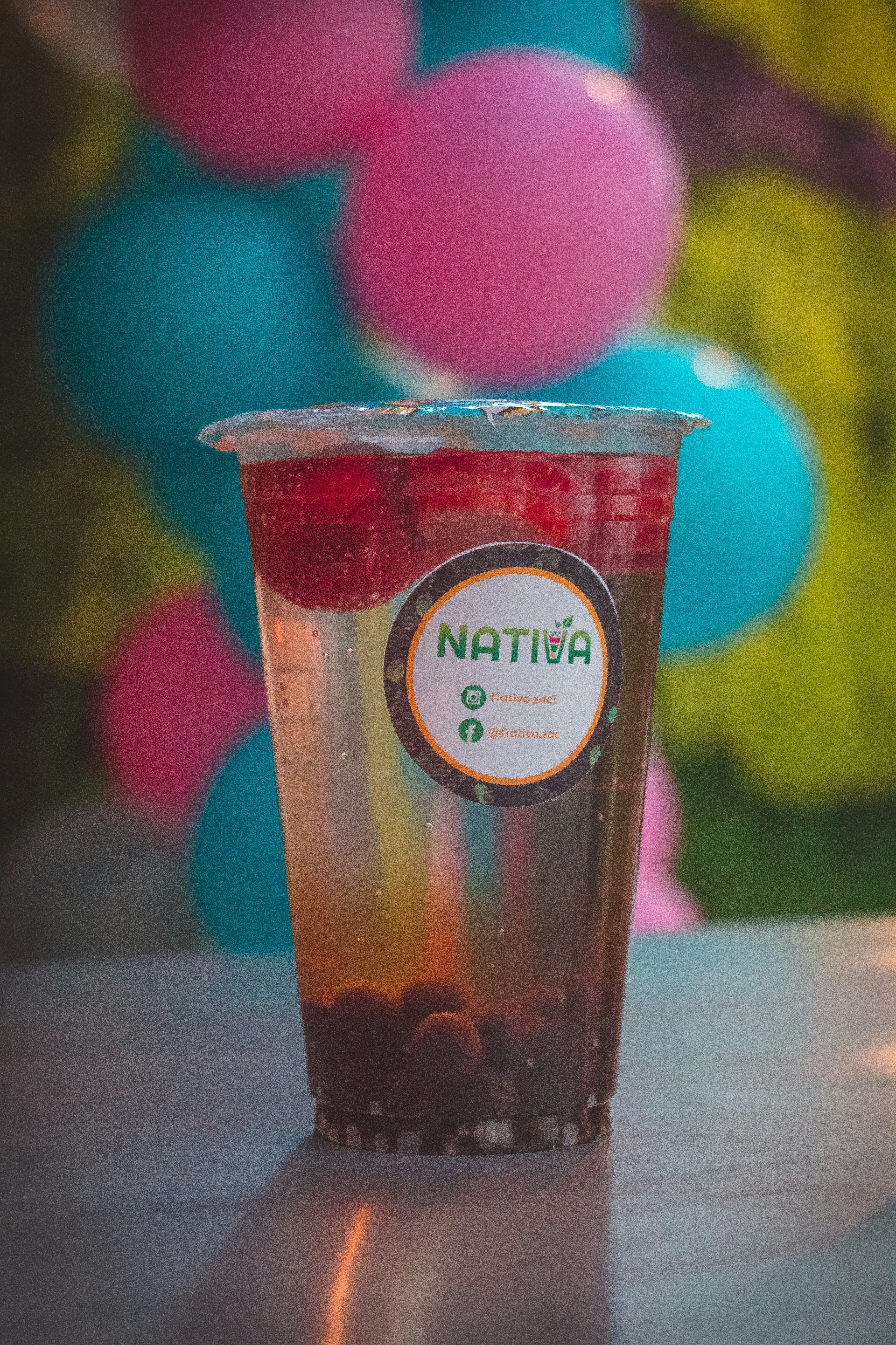 Pink bubble tea drink with colorful popping boba pearls in a clear cup, bright pastel background