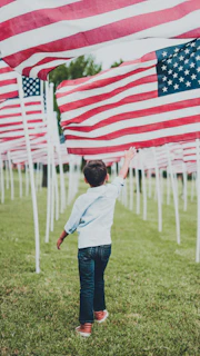 boy in white shirt and blue denim jeans holding us a flag