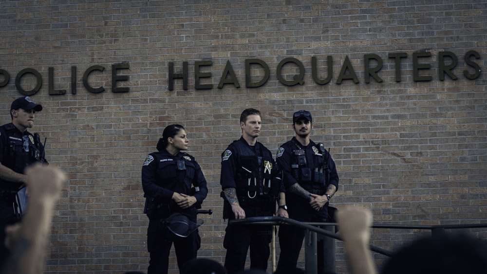 3 men in black uniform standing beside brown brick wall