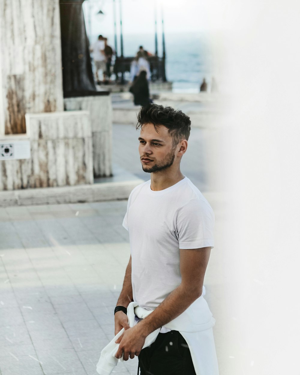 man in white crew neck t-shirt standing on sidewalk during daytime