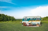 A bright red vintage trailer tent parked on a grassy field, framed by tall trees and a pencil-textured white sky.