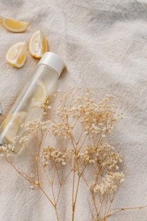 A close-up of a hand holding a clear water bottle with fresh lemon slices inside, sunlight filtering through a kitchen window.