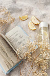 An open book, lemon slices, and a water bottle on a beige linen cloth