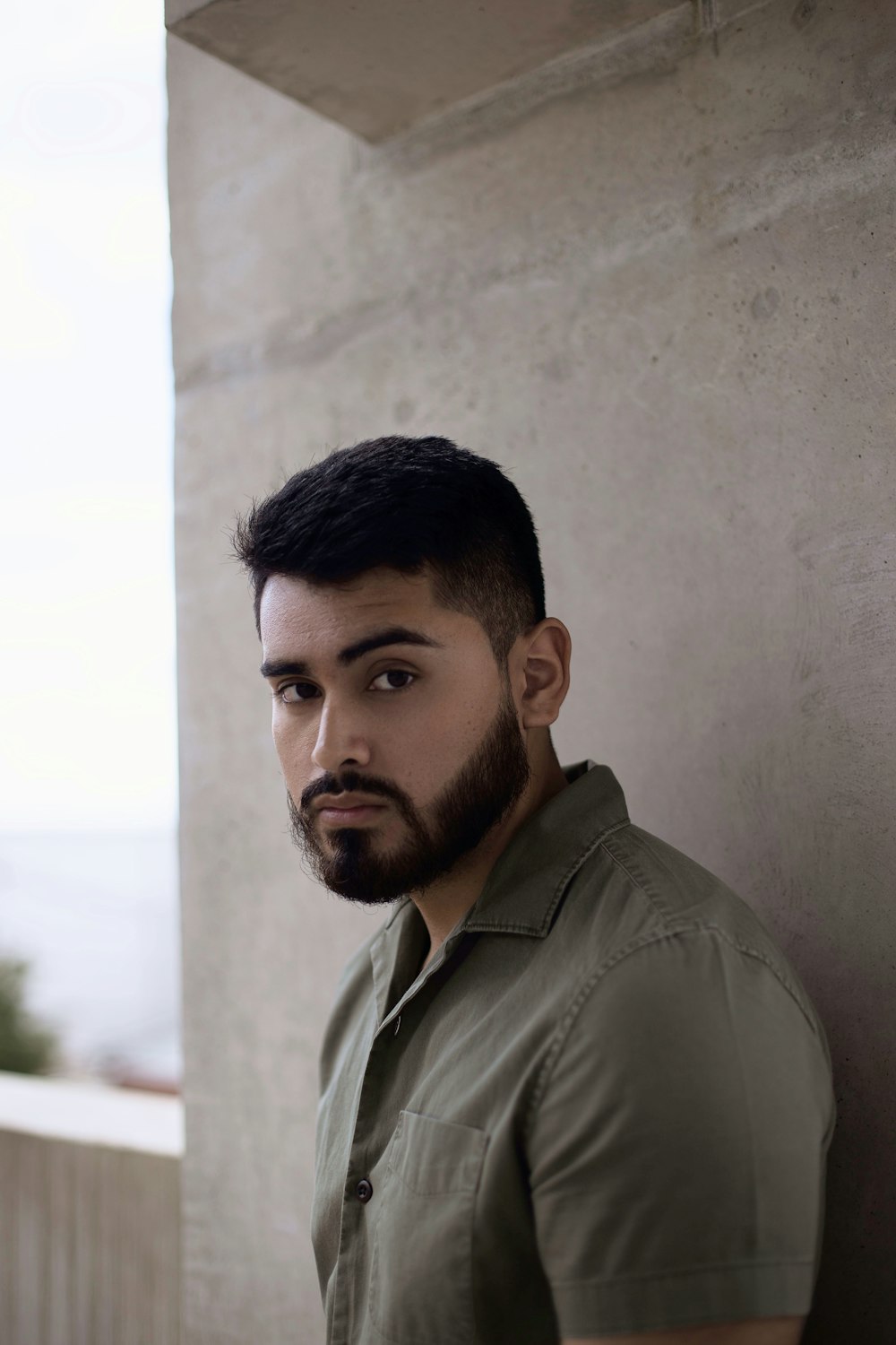 man in brown button up shirt standing beside white concrete wall during daytime