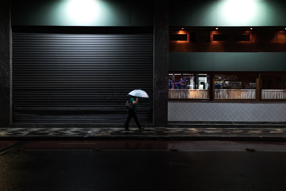 person in black jacket holding umbrella walking on sidewalk during daytime