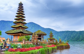 brown and green temple near lake and green mountain under blue sky during daytime