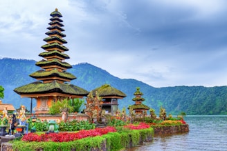 brown and green temple near lake and green mountain under blue sky during daytime