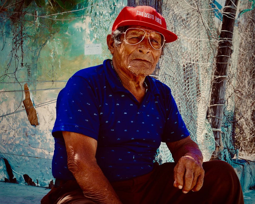 man in blue polo shirt and red cap sitting on brown wooden chair
