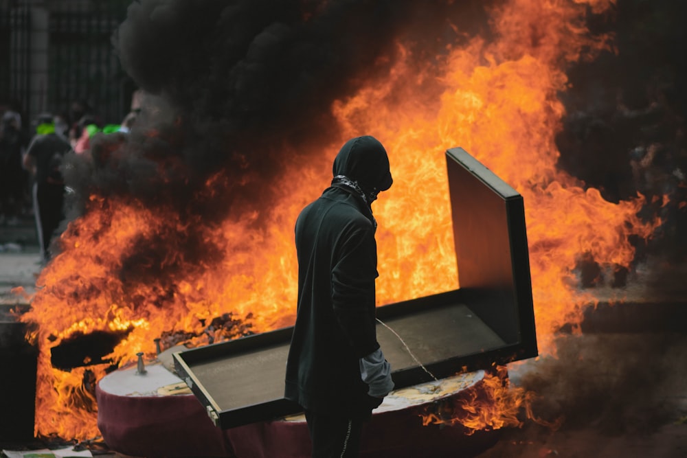 man in black hoodie standing in front of fire
