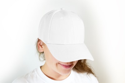 woman in white crew neck shirt wearing white cap cap teams background