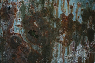 A textured surface covered with rust and corrosion, showing various shades of brown, orange, and gray. The uneven surface and patterns suggest extensive weathering over time.