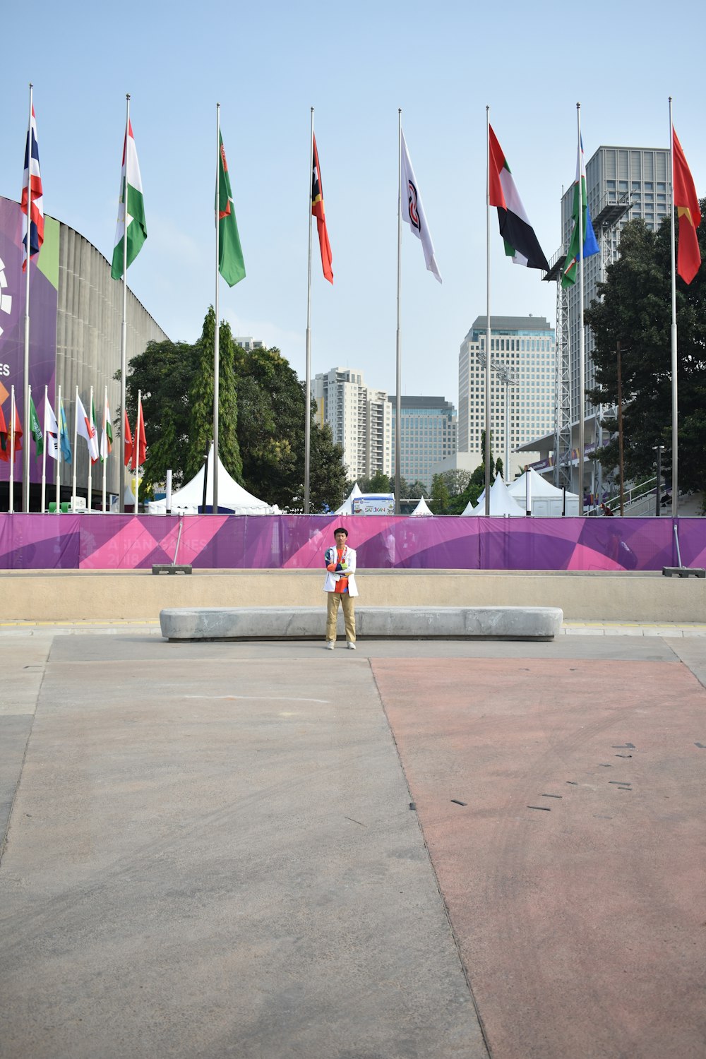 woman in white tank top and pink pants standing on gray concrete pavement near flags