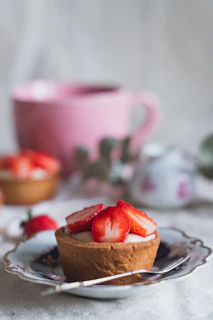 A soft pink tart adorned with fresh berries and a dusting of powdered sugar on a beige linen cloth.