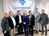 A group of seven individuals is standing in front of a banner with the ACM SIGCHI logo and text. They are dressed in business or casual attire, with varied expressions on their faces.