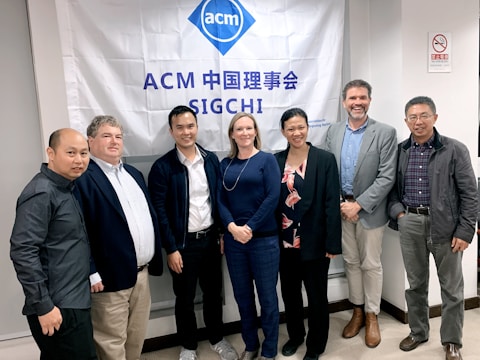 A group of seven individuals is standing in front of a banner with the ACM SIGCHI logo and text. They are dressed in business or casual attire, with varied expressions on their faces.