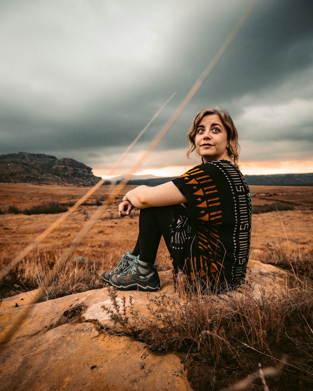 woman in black and white shirt sitting on brown rock during daytime