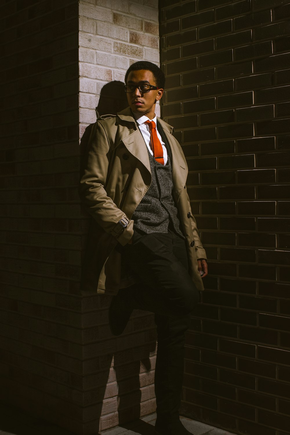 man in brown coat standing beside brick wall