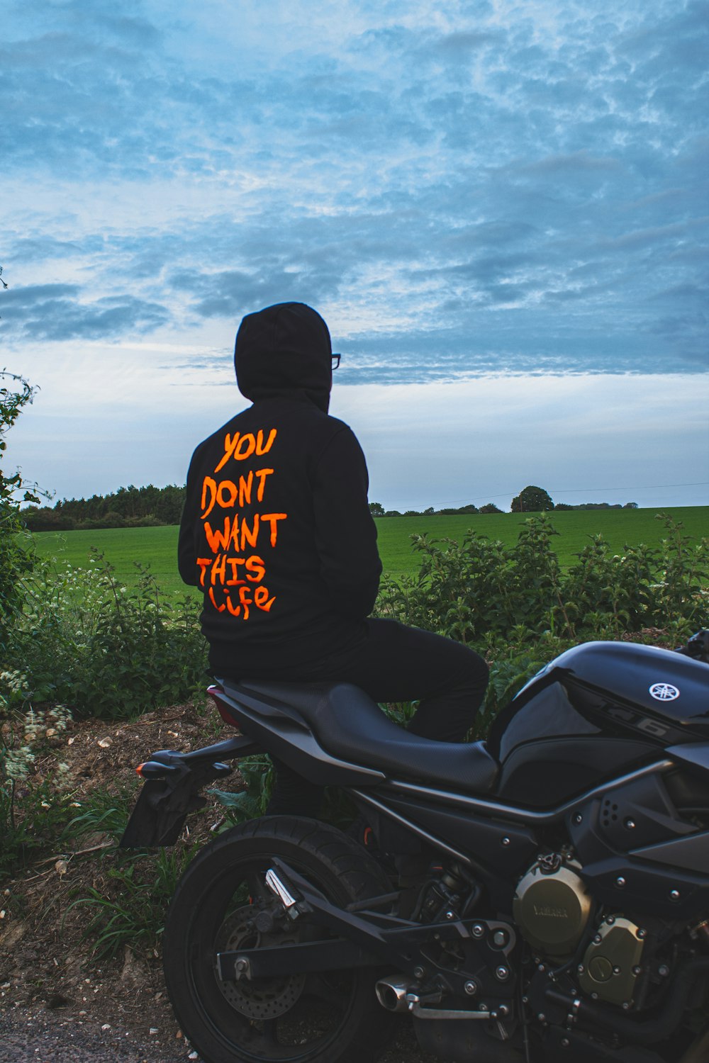 man in black hoodie riding motorcycle on green grass field during daytime