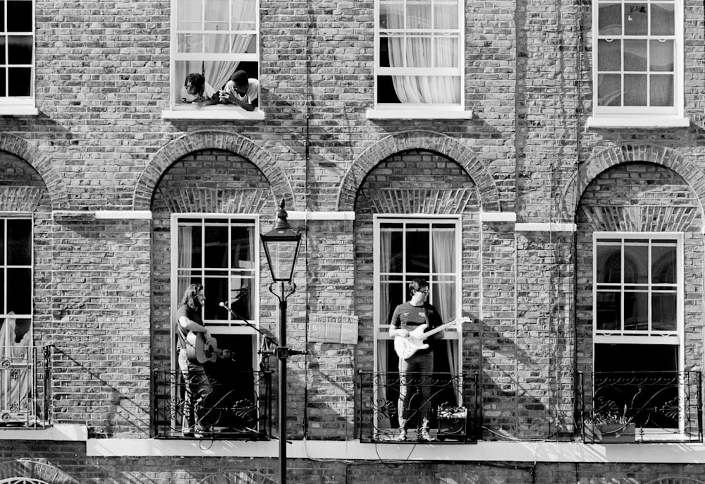 grayscale photo of 2 women sitting on chair near brick building