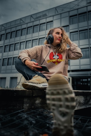 woman in brown hoodie and gray pants sitting on concrete bench during daytime