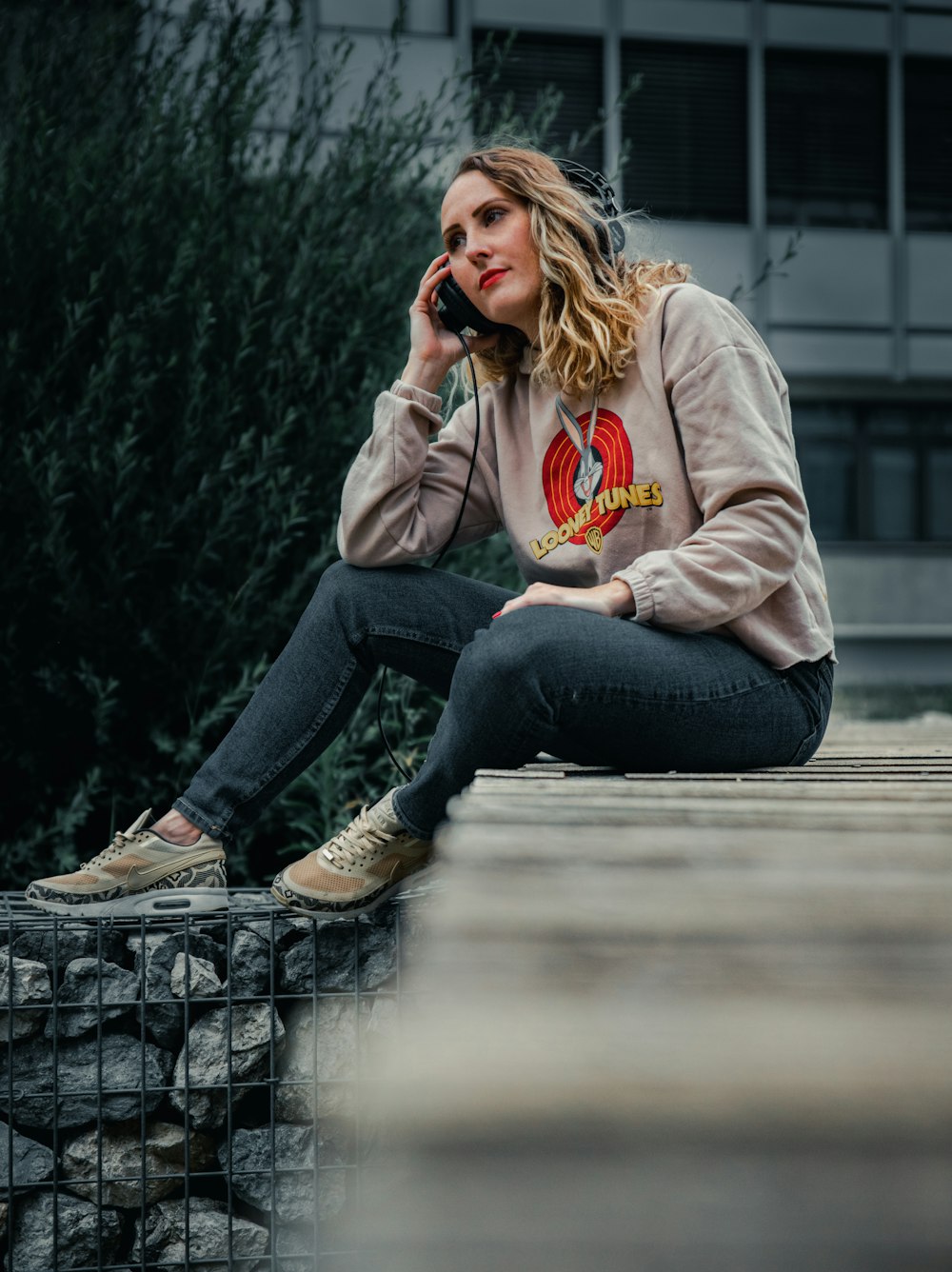 woman in gray hoodie and blue denim jeans sitting on concrete bench