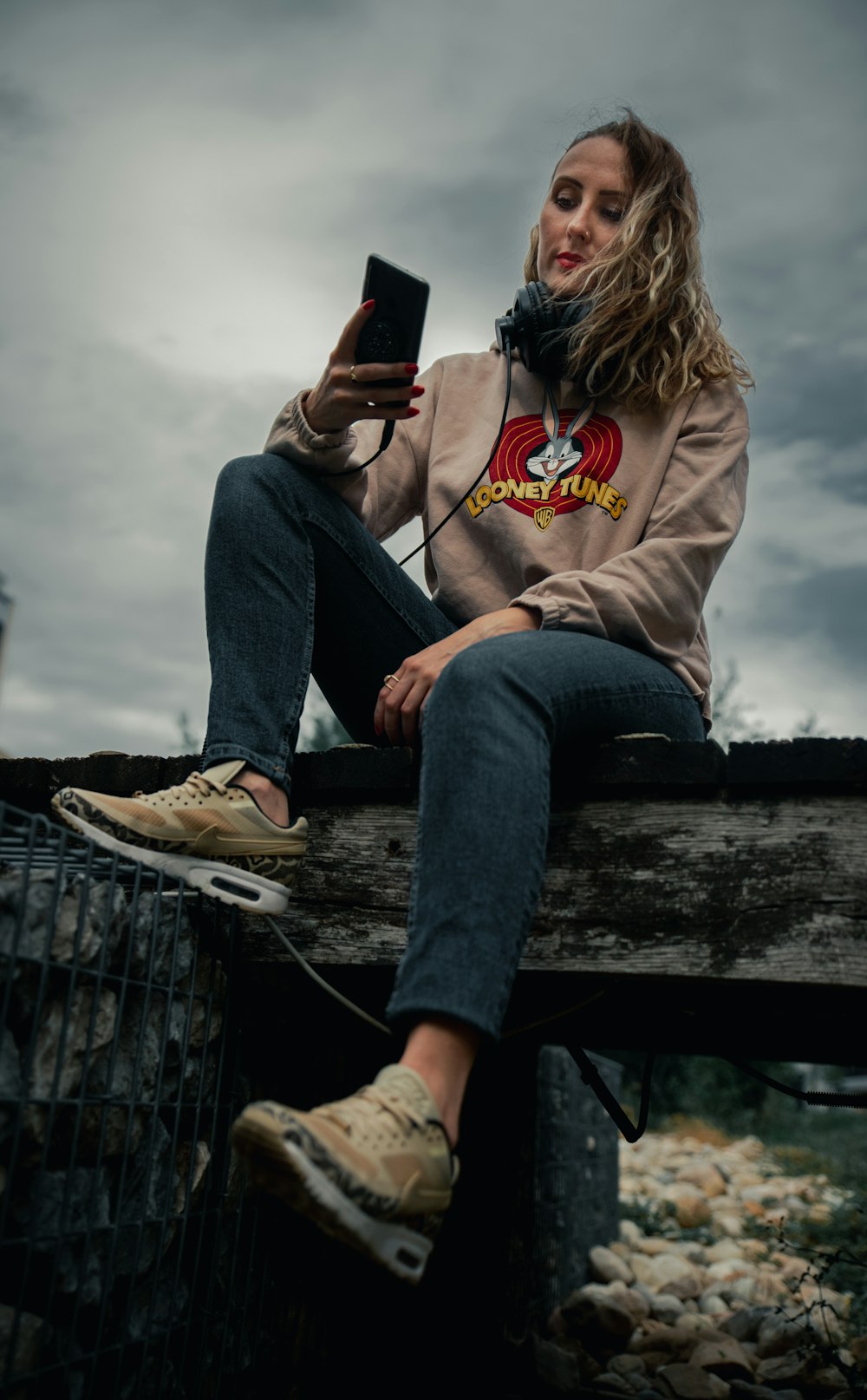 woman in gray hoodie and blue denim jeans sitting on wooden bench