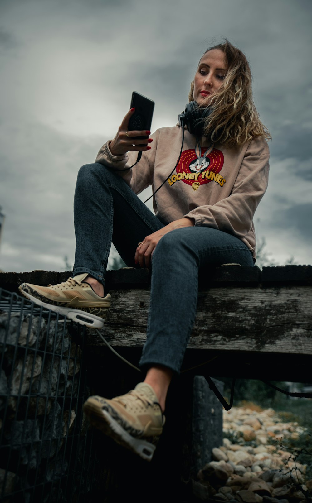 Frau in grauem Hoodie und blauer Jeans sitzt auf Holzbank