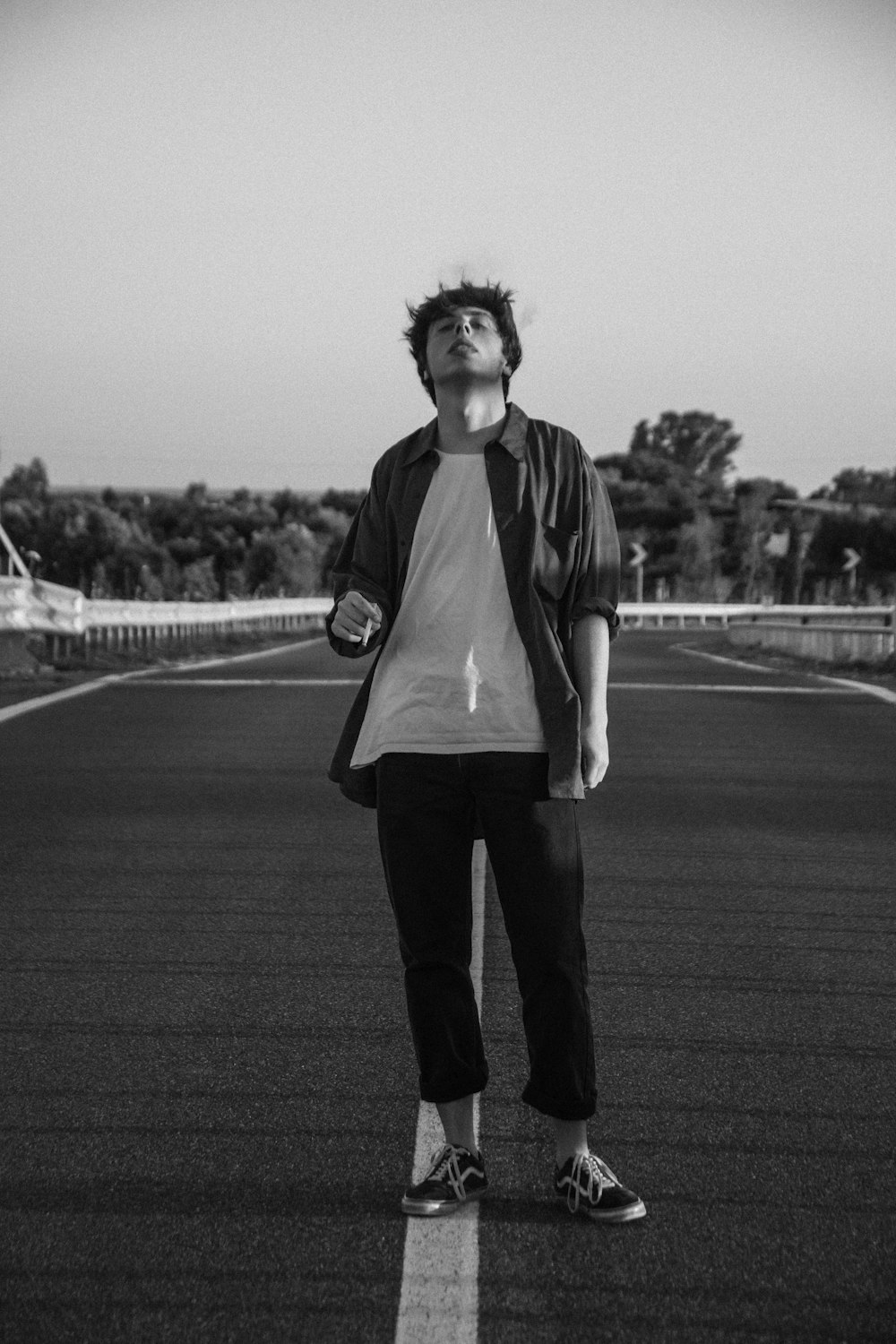 grayscale photo of woman in white shirt and black pants standing on road