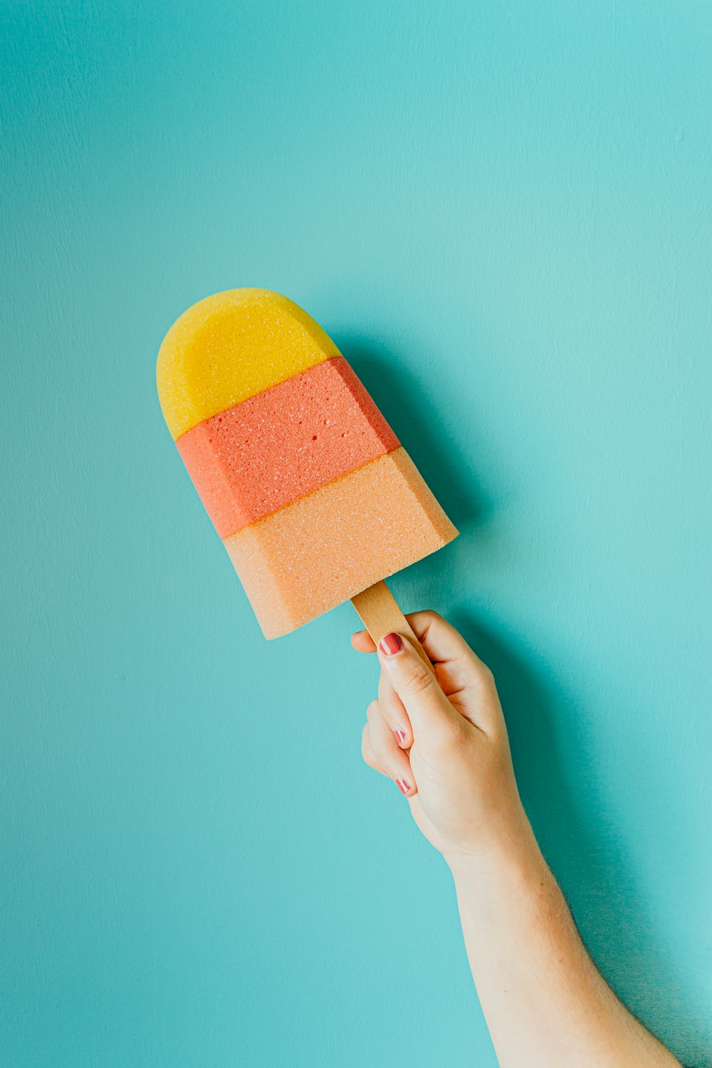 person holding yellow and pink popsicle