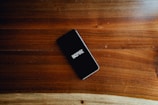 A smartphone with a black screen displaying the word 'INSPIRE' in white text is placed on a smooth wooden surface with visible grain patterns.