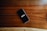 A smartphone with a black screen displaying the word 'INSPIRE' in white text is placed on a smooth wooden surface with visible grain patterns.