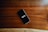 A smartphone with a black screen displaying the word 'INSPIRE' in white text is placed on a smooth wooden surface with visible grain patterns.