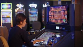 A person is seated at a slot machine console in a casino, focusing intently on the game displayed on the screen. The background shows several other illuminated gaming machines, adding a vibrant and colorful atmosphere to the scene.