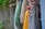 A collection of fishing nets of various colors hang against a rustic stone wall. The nets are adorned with red and turquoise floats, featuring shades of yellow, green, blue, and brown threads. Some parts of the wall have moss and plants, adding a natural touch.