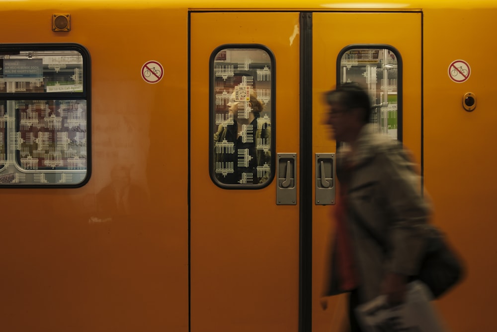 man in gray coat standing beside yellow train