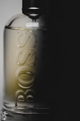 A glass bottle with the word 'BOSS' embossed vertically. The bottle has a sleek, minimalist design and is partially cast in shadow, suggesting a sophisticated and modern aesthetic.