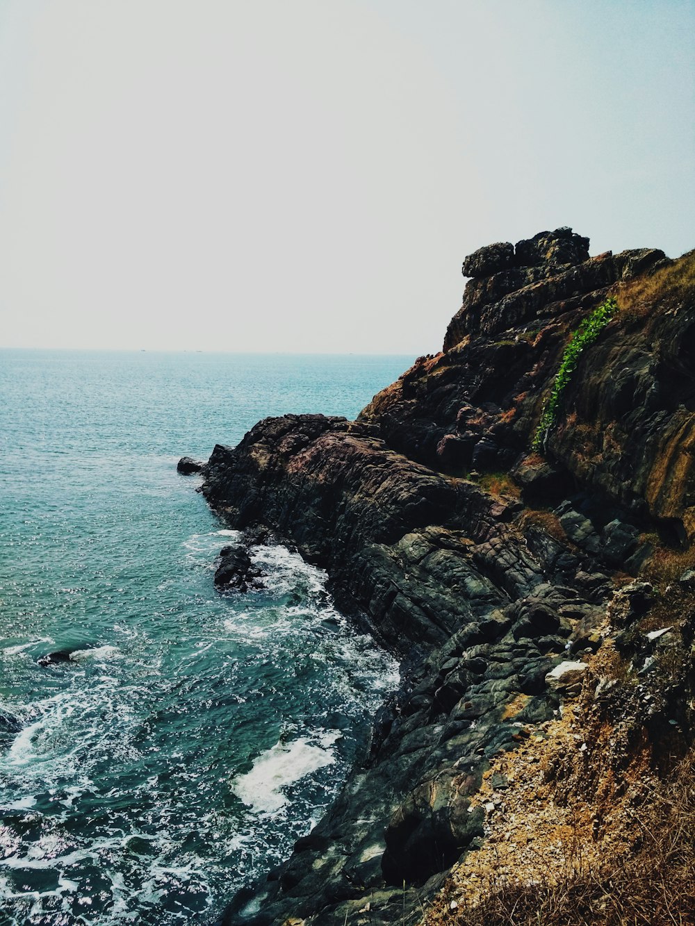 brown and green rock formation beside body of water during daytime