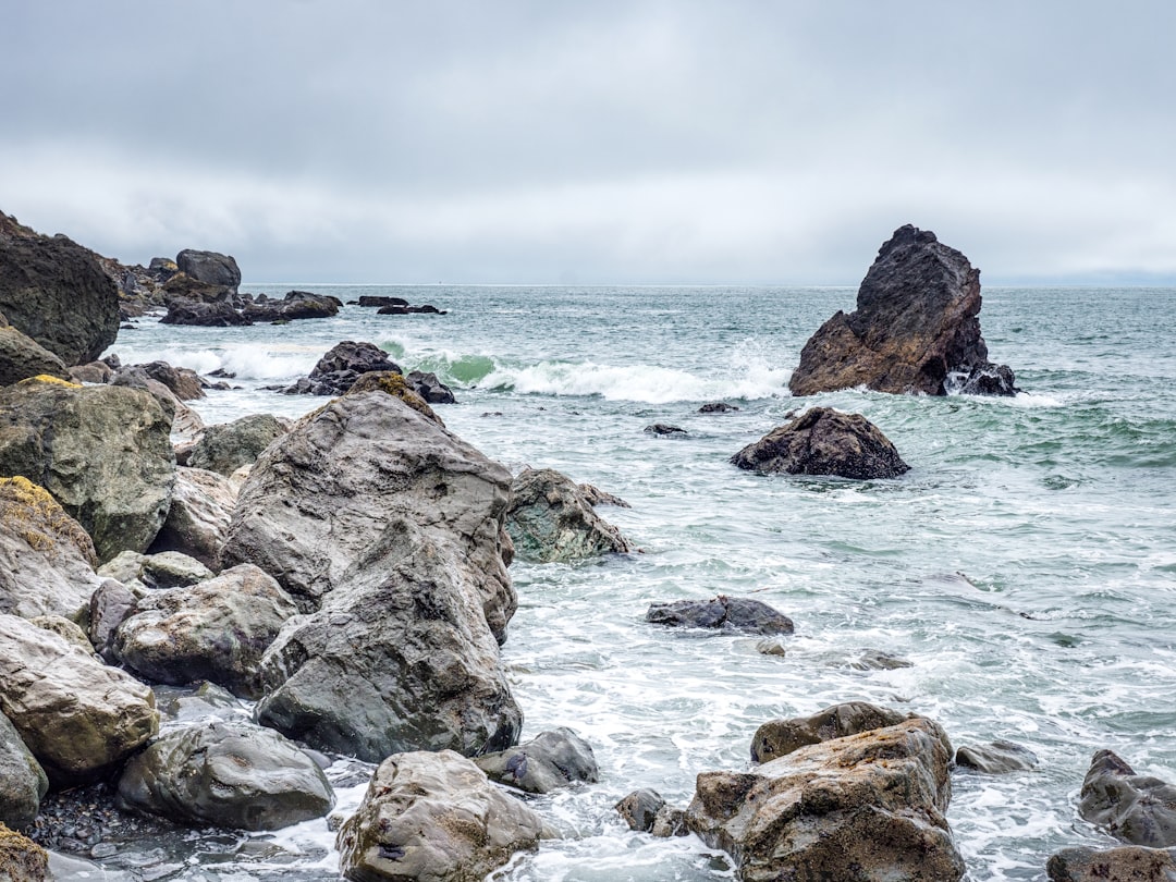 brown rock formation on sea under white clouds during daytime