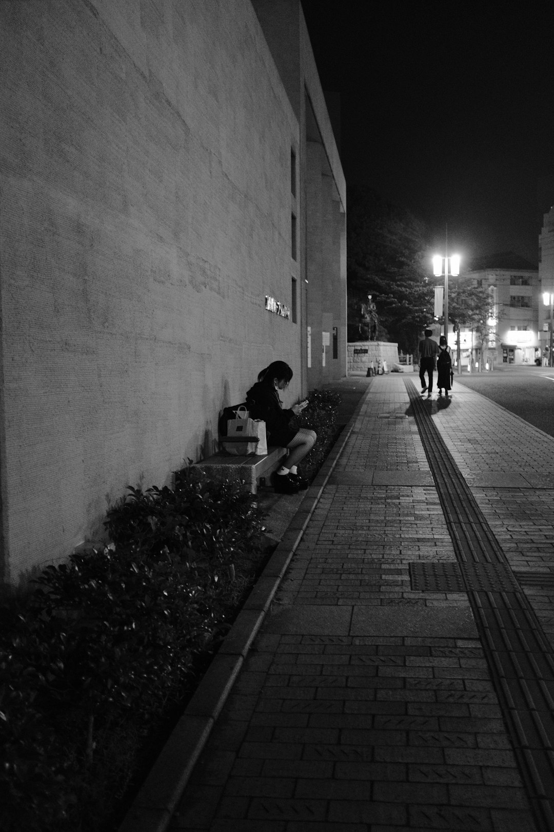 grayscale photo of man sitting on sidewalk