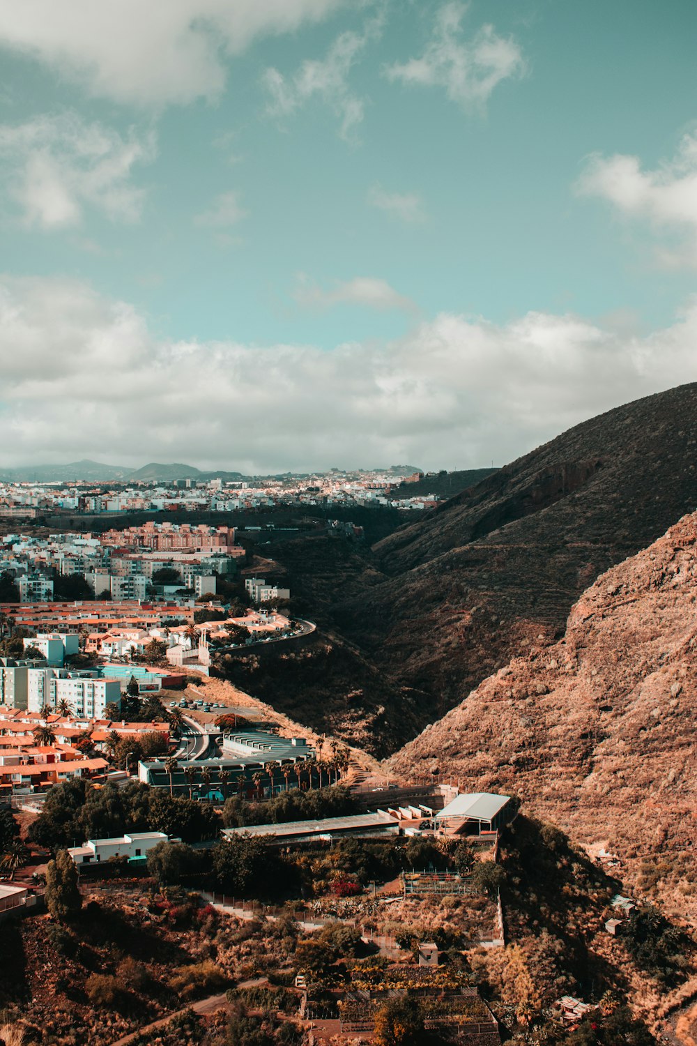 brown and white concrete buildings near brown mountain under white clouds during daytime