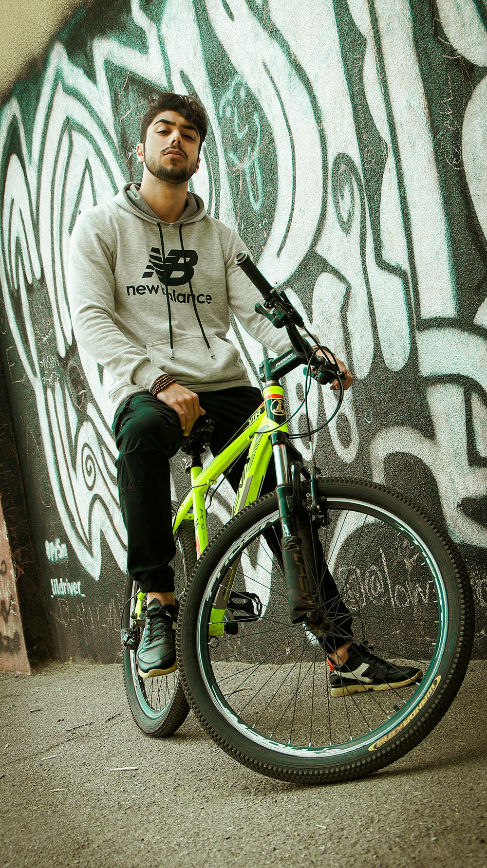 boy in gray hoodie and black pants riding on black and green mountain bike