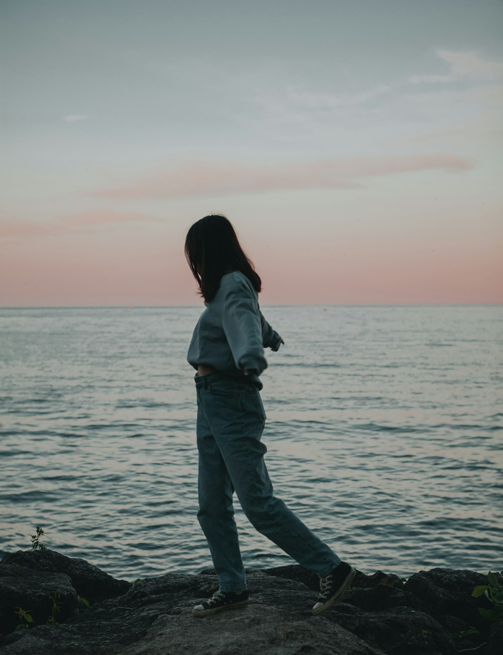 woman in gray jacket and black pants standing on sea shore during daytime