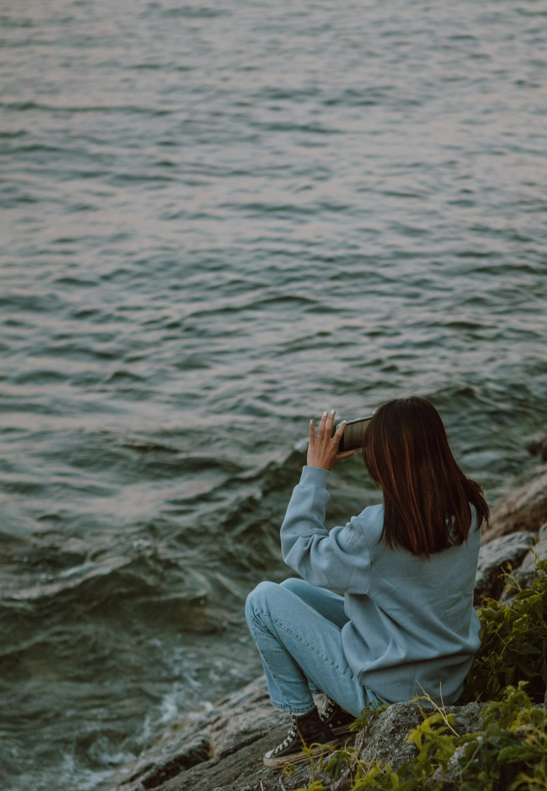 woman in white hoodie sitting on rock near body of water during daytime