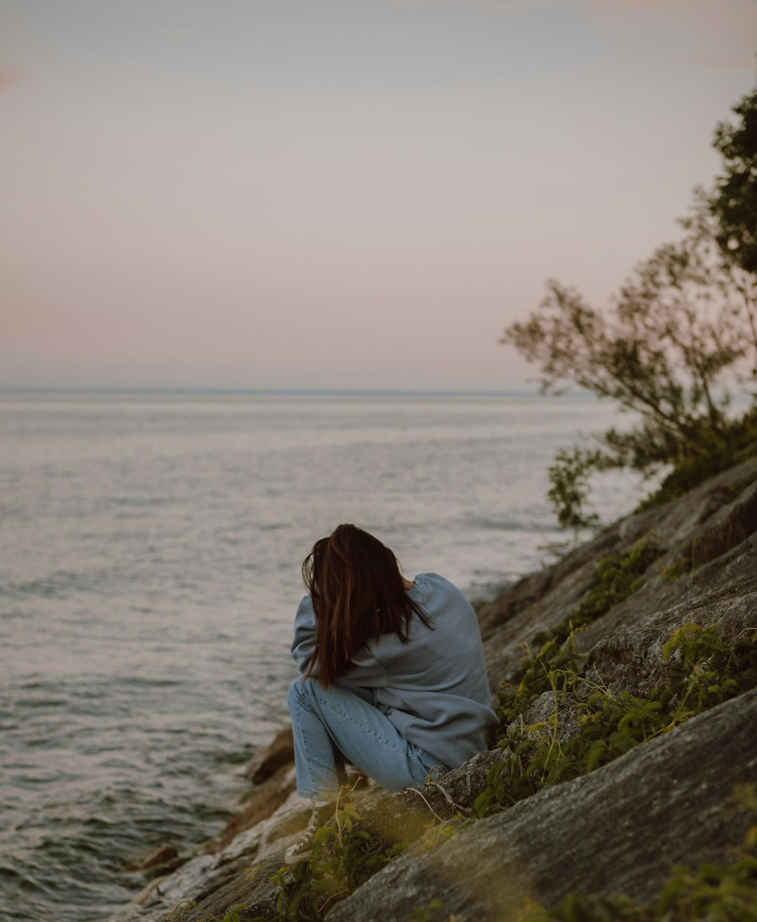 woman in white long sleeve shirt sitting on brown rock near body of water during daytime