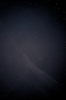 A dark night sky filled with numerous small, faint stars scattered across the expanse. A subtle, dimly lit nebula-like structure is visible, adding a sense of depth and mystique.